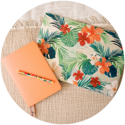 A notebook with a tropical print and a pen on a bed.