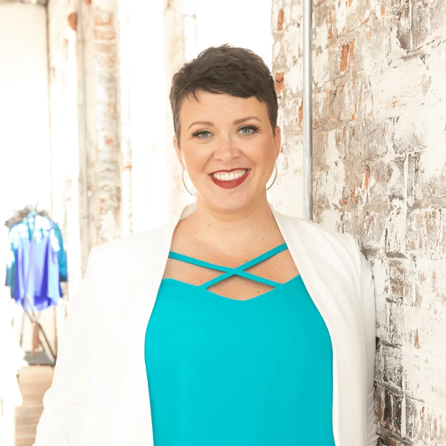 A woman standing in front of a brick wall wearing a blue top.